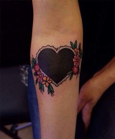 a heart tattoo with flowers around it on the forearm and hand, in front of a woman's arm