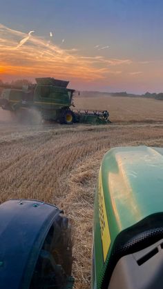 the sun is setting over a farm field with two combiners working on it's crops