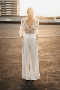 a woman standing in an empty parking lot with her hands on her hips wearing wide legged white pants