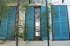 blue shutters on the side of a building with a tree growing out of it