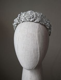 a white headpiece with flowers and leaves on it's side, sitting on top of a mannequin