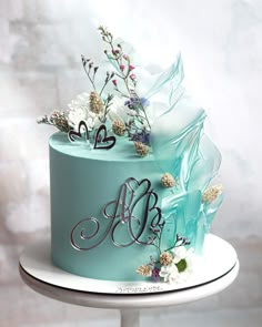 a blue wedding cake with flowers and monogrammed letters on top is sitting on a white plate