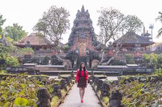 a woman standing in front of a building with lots of plants and trees around it