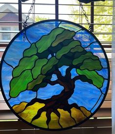 a circular stained glass window with a tree in the center, hanging from a chain