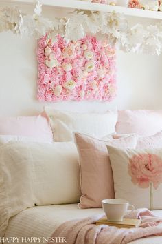 a white bed topped with lots of pillows and pink flowers next to a wall hanging