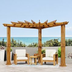 a wooden gazebo sitting on top of a stone patio next to the ocean with two chairs and a table