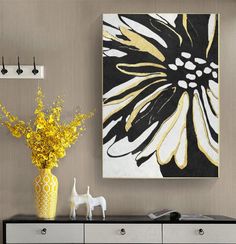 a vase filled with yellow flowers sitting on top of a black and white dresser next to a painting