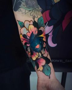 a person with a colorful tattoo on their arm and wrist, holding up a flower