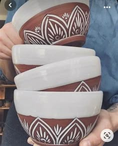 someone holding three bowls in their hands with designs painted on the bottom one is brown and white