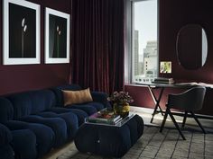 a living room with red walls and blue couch in front of a table, two framed pictures on the wall