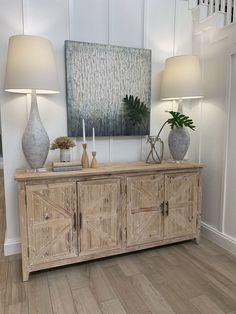 a wooden sideboard with two lamps and a painting on the wall in the background