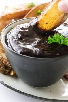 a hand dipping some kind of sauce in a bowl with bread and other food on the side