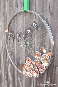 a bicycle wheel hanging on the side of a wooden fence with flowers in front of it