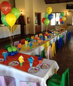 the tables are set up for a birthday party with colorful balloons and cups on them