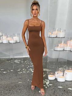 a woman standing in front of candles wearing a brown dress with spaghetti straps and low neckline