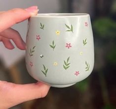 a hand holding a cup with flowers painted on it