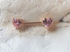 two heart shaped pink crystals are attached to a gold barbell earring that sits on a rock