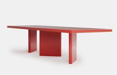 a red table sitting on top of a white floor next to a gray wall with an orange base