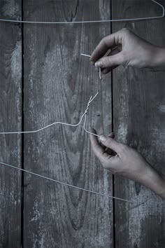 two hands that are holding some string on a wooden surface with one hand reaching for the string