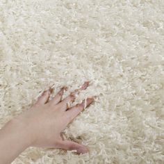 a person's hand reaching for something on the floor with white shag carpet