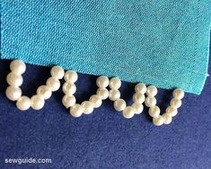 the word love spelled out with beads on a blue fabric background in closeup view