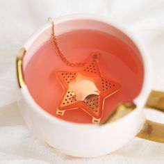 a star shaped tea in a white cup with gold handles and a chain hanging from it