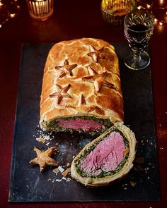 a roast beef sandwich cut in half on a cutting board next to a glass of wine