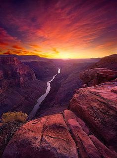 the sun is setting at the edge of a canyon with a river running through it