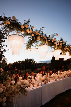 a long table is set with flowers and candles for an outdoor wedding reception in the evening