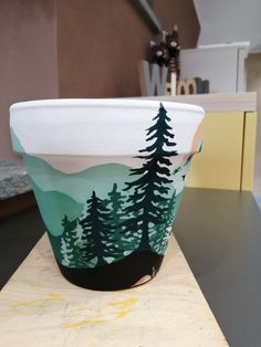 a bowl with trees painted on it sitting on top of a wooden table next to a counter