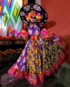 a woman in a colorful dress and hat with flowers on her head is posing for the camera