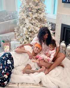 a woman and two children are sitting on a bed in front of a christmas tree