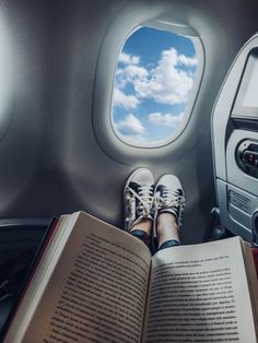 a person is reading a book while sitting in an airplane with their feet up on the seat