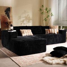 a living room filled with black couches and pillows on top of a white rug