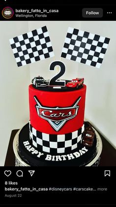 a red and black cake with two cars on it's top is decorated with checkered flags