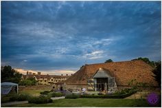 an old building with a thatched roof and garden in the foreground, under a cloudy sky