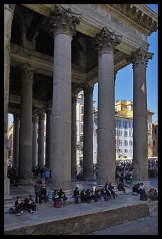 many people are sitting on the steps in front of large columns