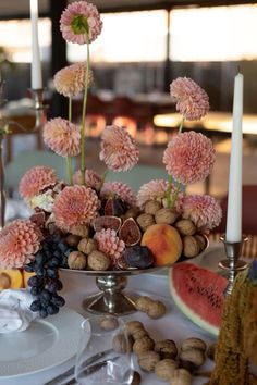 an arrangement of flowers, fruit and candles on a table set for a formal dinner