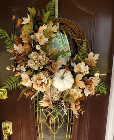 a wreath on the front door with flowers and leaves hanging from it's side