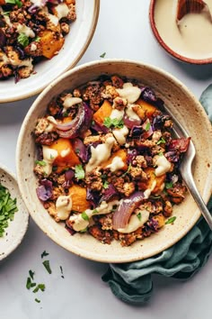 two bowls filled with food on top of a white table next to other plates and utensils