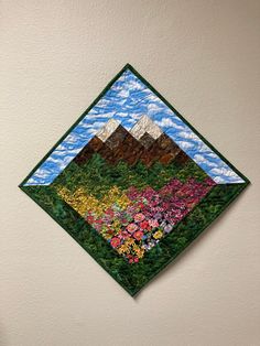 a wall hanging on the side of a white wall with flowers and mountains painted on it