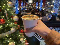 a person holding a cup of coffee in front of a christmas tree with lights on it