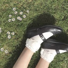 a woman's legs in white socks and black shoes on grass with daisies