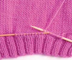 the knitting needle is next to an unpainted pink knitted sweater