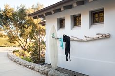 there is a surfboard hanging on the wall next to a white house with trees in the background