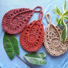 three crocheted purses sitting on top of a blue towel next to a plant