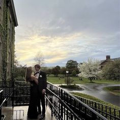 a man and woman are standing on a balcony in front of a building with trees