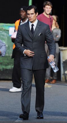 a man in a suit and tie walking down the street while holding a water bottle