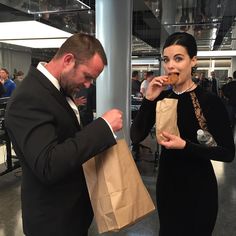 a man and woman are eating food in an office building with other people standing around