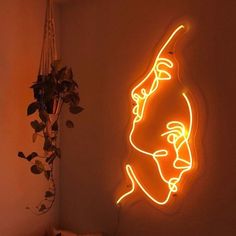 a neon sign with a woman's face on the wall next to a potted plant